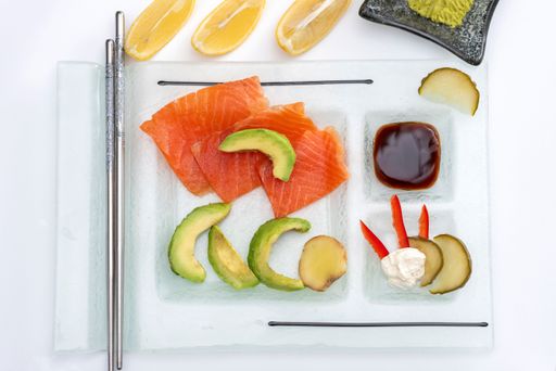 A closeup of a Fresh rolled smoked salmon on a rectangular plate with wasabi avocado, cheese, lemon pickles and soy sauce