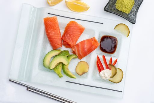 A closeup of a Fresh rolled smoked salmon on a rectangular plate with wasabi avocado, cheese, lemon pickles and soy sauce