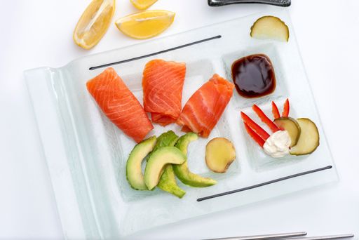 A closeup of a Fresh rolled smoked salmon on a rectangular plate with wasabi avocado, cheese, lemon pickles and soy sauce