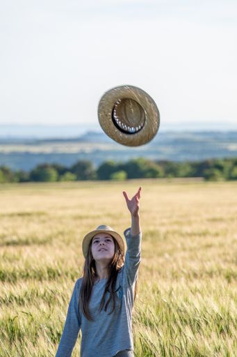 A vertical shot of a young female throwing a hat on an agricultural farm