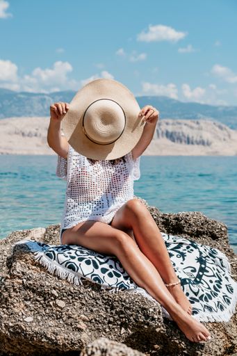 A vertical shot of a beautiful sexy woman with a hat and sunglasses enjoying summer sea