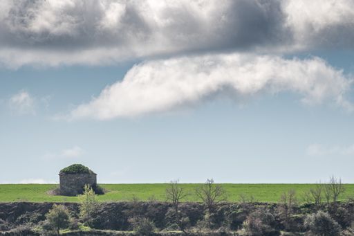 A small farmer's stone hut on a green cereal field under cloudy sky