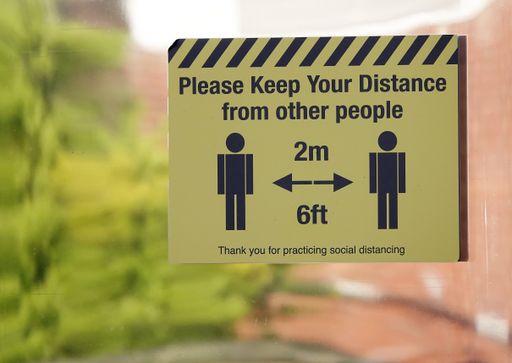 A closeup of a yellow sign outside advising social distancing and warning about dangers of covid-19