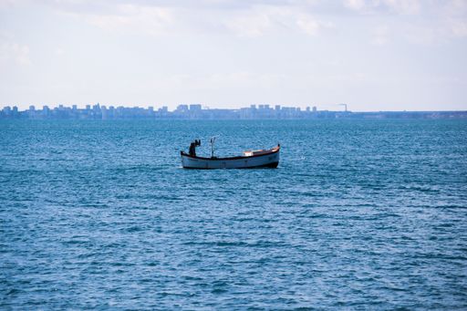 A panoramic shot of a calm ocean with a boat under cloudy skies  with a city skyline in the background