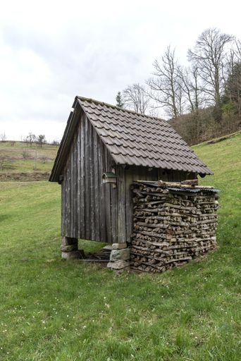 A vertical shot of a small wooden shed in a green field during daylight
