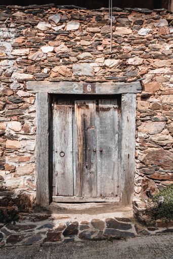 A closeup of the number six sign on the old weathered small wooden door of a stone building
