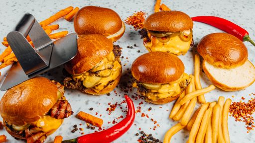 A closeup shot of tasty smash burgers, French fries, and red spicy pepper on the white background