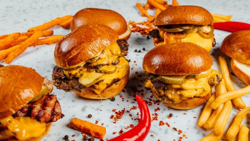 A closeup shot of tasty smash burgers, French fries, and red spicy pepper on the white background