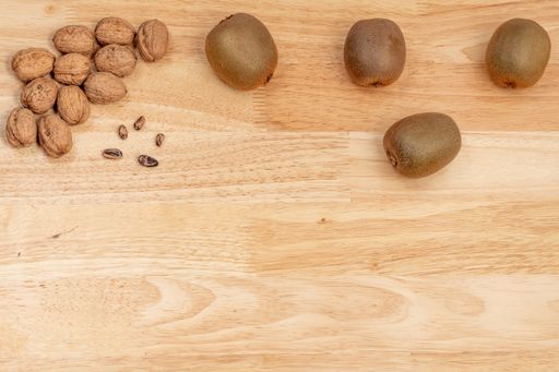 A top view of walnuts, kiwis, and pine nuts on a wooden table