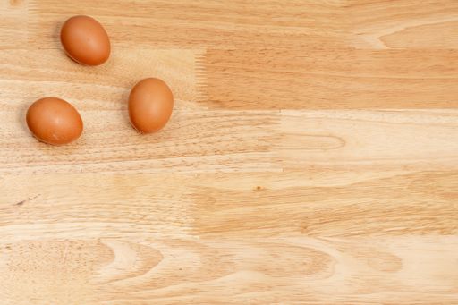 Three eggs on the upper left corner of the wooden table with copy space