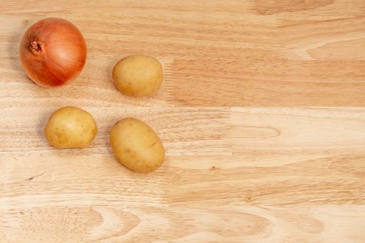 A top view of onion and potatoes on a wooden table with space for text