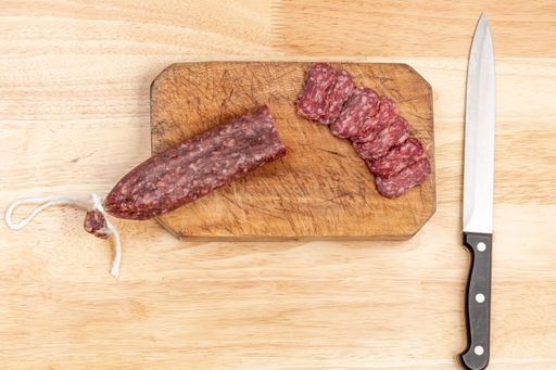 A top view of sausage cut on a wooden board with a knife on a wooden table