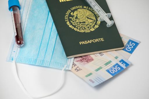 A syringe needle with cash bills and a Mexican passport on the table with a facemask and a covid-19 blood test sample on it