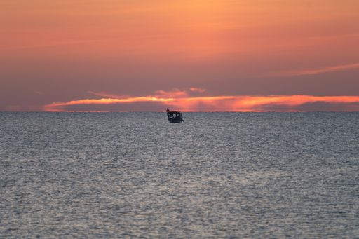 A silhouette fishing boat swimming in the Mediterranean sea during sunset