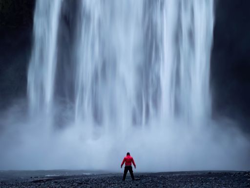 A man standing by a massive waterfall on the shore in Skogafoss, Iceland