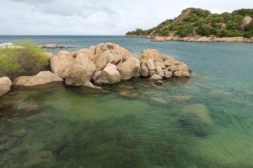 The sea surrounded by rocks covered in greenery under a cloudy sky at daytime
