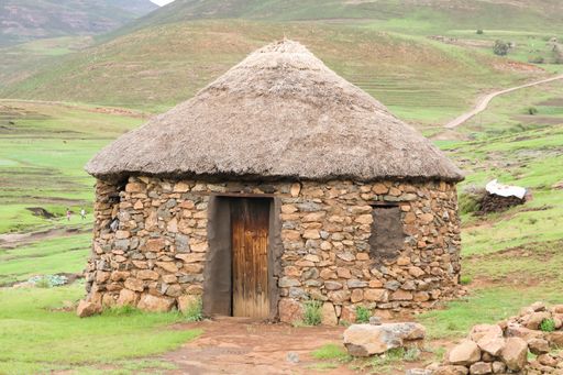 A stone hut with a bamboo roof surrounded by rocks and hills covered in greenery