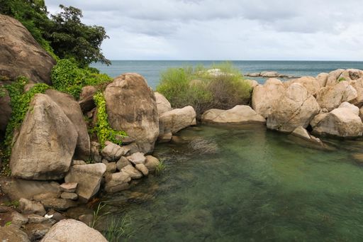 The sea surrounded by rocks covered in greenery under the cloudy sky