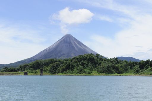 A closeup shot of the Arenal volcano peak and a lake with forests on the shore in the foreground