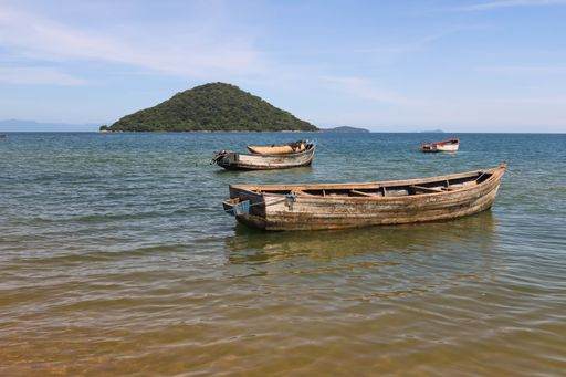 The sea with wooden boats on it surrounded by hills covered in greenery under the sunlight