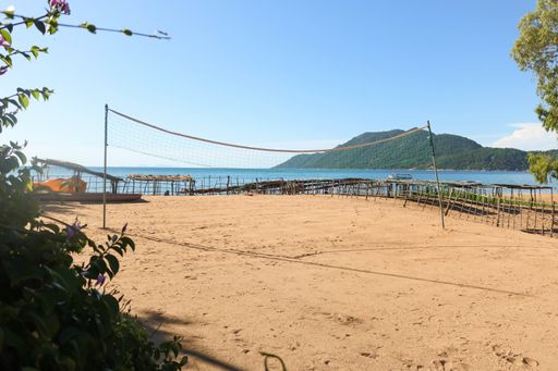 A volleyball net on the beach surrounded by the sea and hills covered in greenery under the sunlight