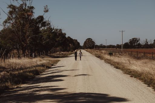 A road surrounded by fields with two children walking on it during daylight