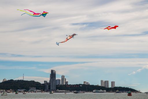 A scenic view of colorful kites flying over Pattaya beach with buildings in the background