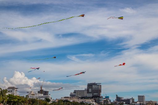 A scenic view of colorful kites flying over Pattaya beach with buildings in the background