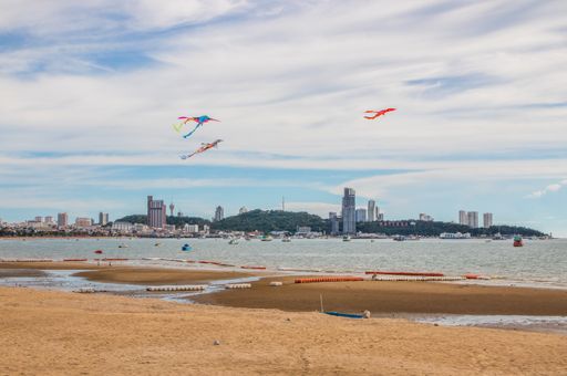 A scenic view of colorful kites flying over Pattaya beach with buildings in the background