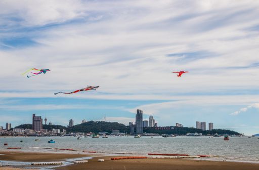 A scenic view of colorful kites flying over Pattaya beach with buildings in the background