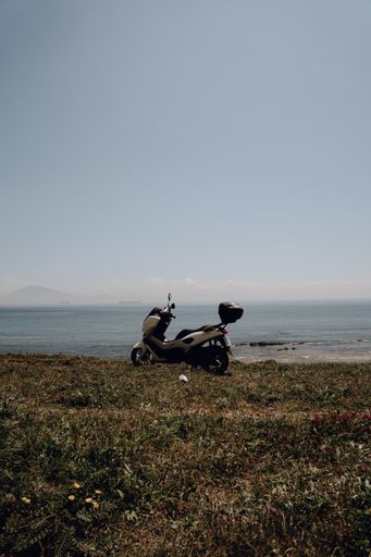 A motorcycle parked on a grassy hill near the seashore under a blue cloudless sky in Tarifa, Spain
