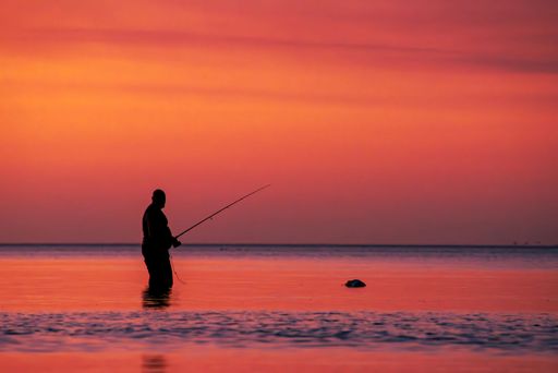 A silhouette of a man fishing at a stunning sunset