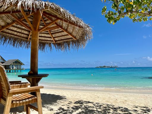 A beach chair is positioned beneath an open umbrella, placed on a sandy shoreline
