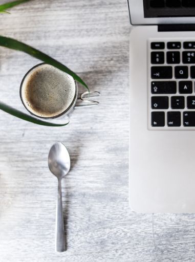 An overhead shot of a laptop with a coffee and a spoon on a wooden table