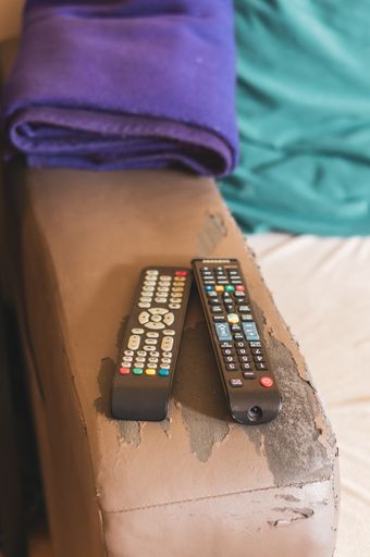 Two remote controllers including Samsung laying on a damaged leather sofa.