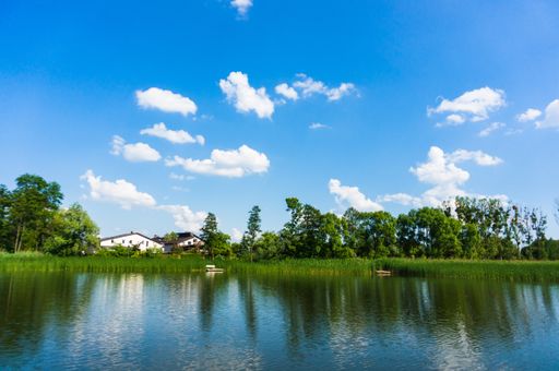 A scenic view of trees reflected on a tranquil river under a cloudy sky in Kornik, Poland
