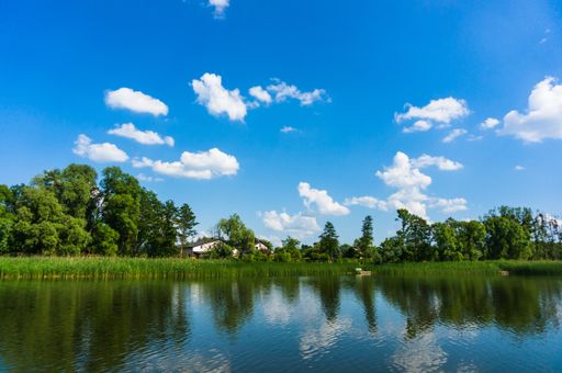 A scenic view of trees reflected on a tranquil river under a cloudy sky in Kornik, Poland