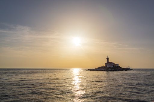 A closeup shot of a lighthouse on the small island in the middle of the sea at sunset