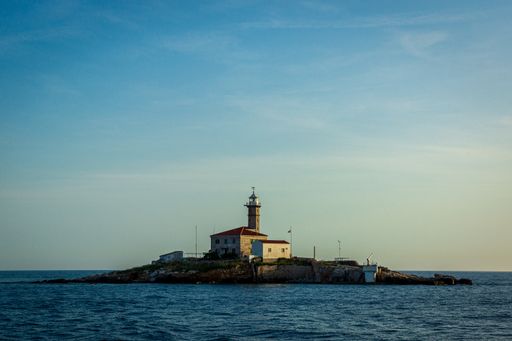 A closeup shot of a lighthouse on the small island in the middle of the sea