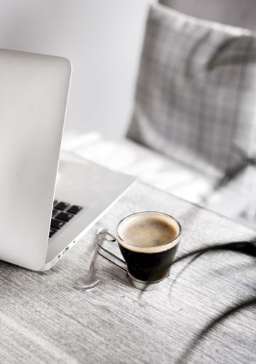 A closeup of a coffee on a table with a spoon and a laptop on the side