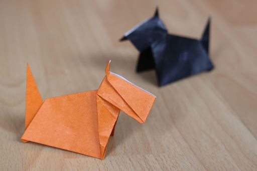 A closeup of an Origami of a brown Scottish terrier dog with a black one in the background