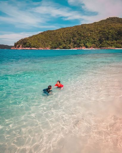 The children swimming in the crystal-clear turquoise waters near a sandy beach
