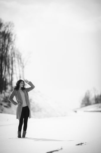 A greyscale shot of a young female in glasses posing on a snowy winter day