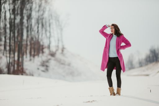 A young female in glasses and a pink jacket posing on a snowy winter day