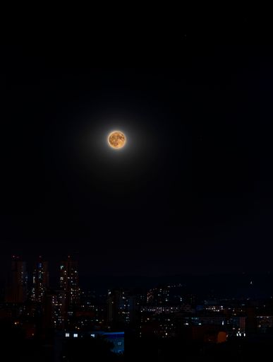 A dramatic night scene with a full moon in the night sky above the silhouettes of tall city buildings