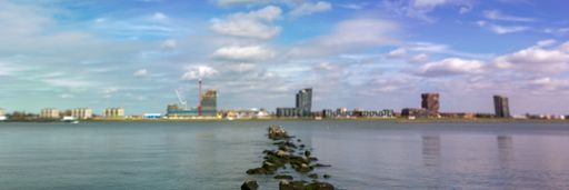 A panoramic shot of seawater with rocks and cityscape on the background under a beautiful cloudscape