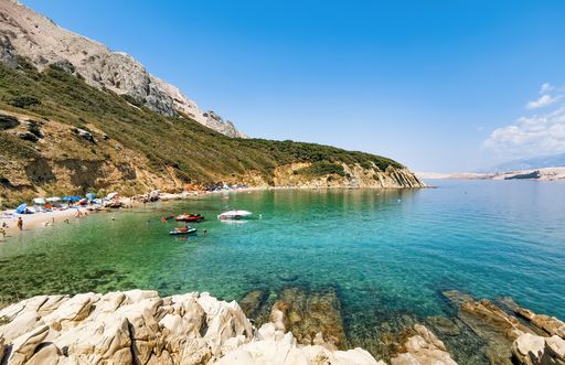 Amazing beach in bay with turquoise sea water. Sunny summer day on Pag island in Croatia. Boats and jet ski moored near beach.