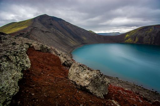 A stunning landscape featuring a large Blahylur 
crater surrounded by brown rocks on a hill