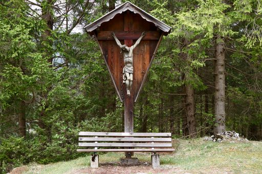 The statue of crossed Jesus Chrised near a bench with a forest in the background