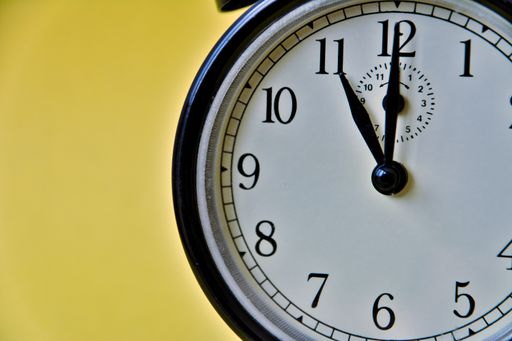 Shot of vintage retro analog clock on showing 11 o clock. Yellow background.